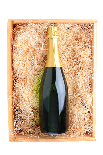Overhead shot of a single champagne bottle in a wood shipping crate filled with packing straw. Vertical format over a white background
