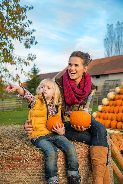 istock Happy mother and child sitting on haystack with pumpkins 530348999
