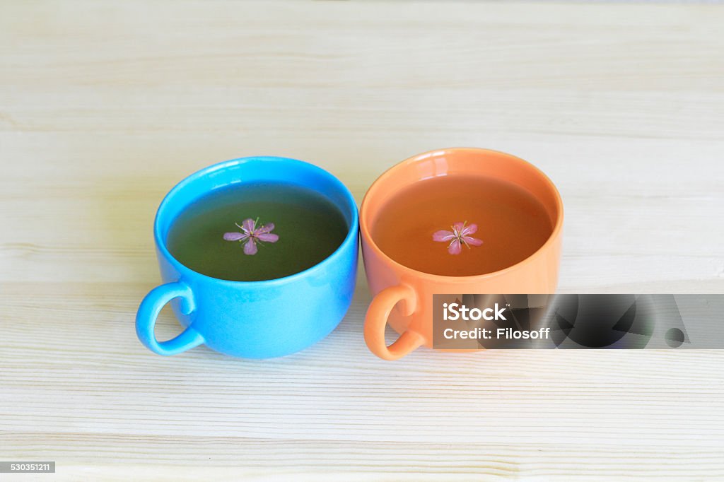 Two colorful tea cups with pink flowers inside Two colorful tea cups with tea and pink flowers inside Blue Stock Photo