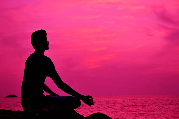 istock Silhouette of young man meditating at sunset - Stock Image 530353865