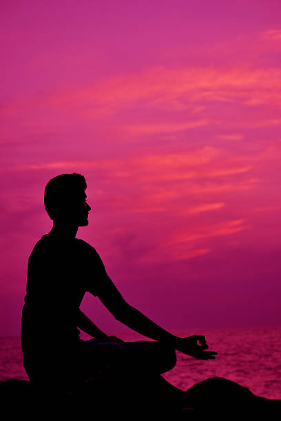 istock Silhouette of young man meditating at sunset - Stock Image 530363567