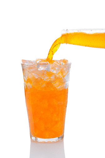 Closeup of a bottle of Orange Soda Pouring into Glass of Ice. Vertical format over a white background with reflection.