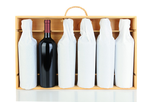 Six tissue wrapped wine bottles in a wooden crate with rope handle. Horizontal format isolated on white with reflection. One bottle is not wrapped.