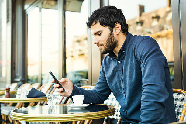 Young Man Browsing Social Media in a Sidewalk Cafe