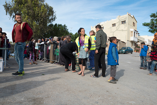 Chios, Greece - May 5, 2016: Refugees are standing in line (or getting ready to stand in line) for being served breakfast Souda refugee camp in Chios Town on Chios Island in Greece. There are two separate lines for women (and children) and men (to the left) The breakfast this day consisted of a sandwich and a boiled egg. The meals are served by volunteers from the Norwegian NGO Drop in the Ocean. The food is paid for by donations collected by the volunteers. At the moment 1,250 refugees are fed each day.