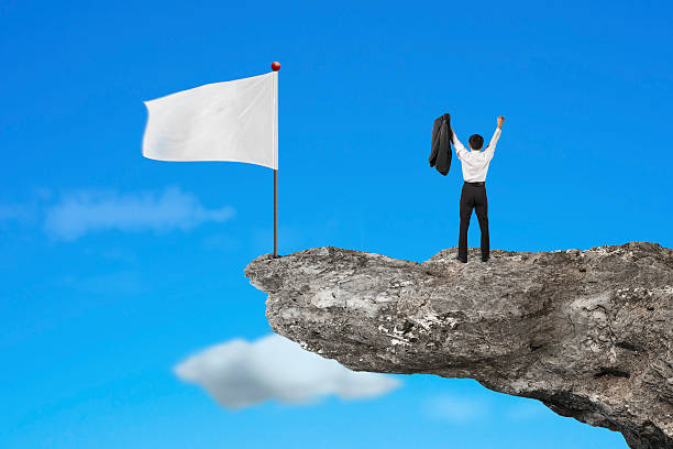 istock man cheering on cliff with blank white flag and sky 530415139