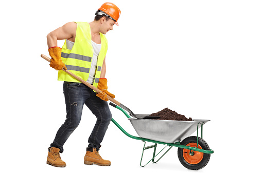 Construction worker loading dirt into a wheelbarrow isolated on white background