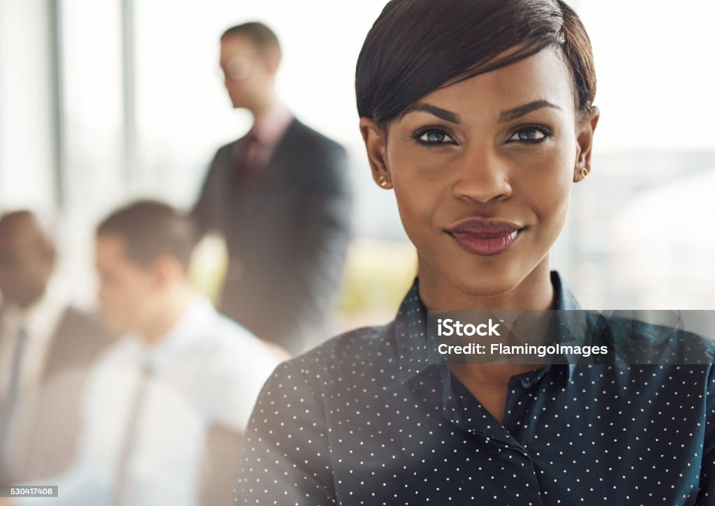 Confident business woman in office with group Close up on smiling beautiful business woman with light flare over shoulder from large window in office with group Leadership Stock Photo