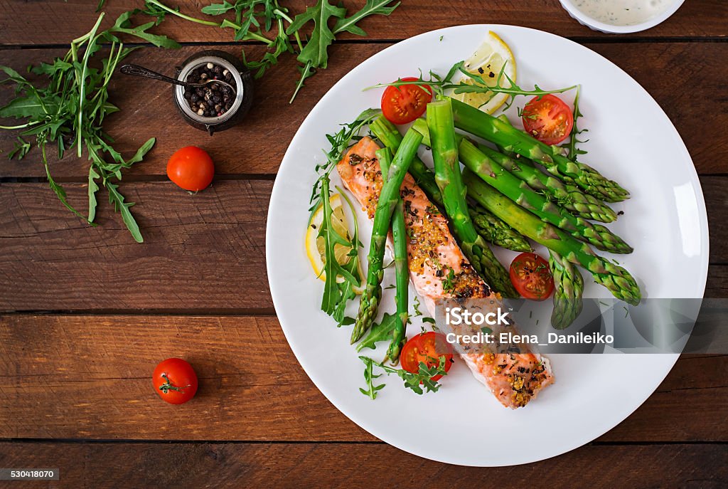 Baked salmon garnished with asparagus and tomatoes with herbs Baked salmon garnished with asparagus and tomatoes with herbs. Top view Salmon - Seafood Stock Photo
