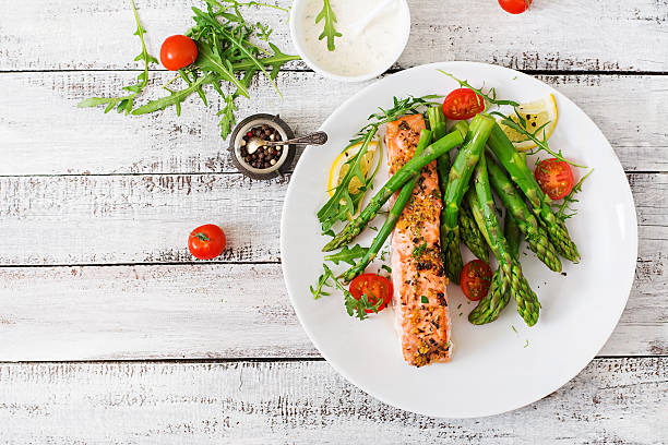 Baked salmon garnished with asparagus and tomatoes with herbs Baked salmon garnished with asparagus and tomatoes with herbs. Top view asparagus photos stock pictures, royalty-free photos & images
