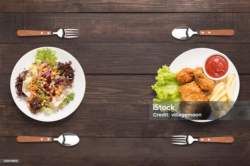 Fresh salad and Fried chicken and french fries. contrasting food. Fresh salad and Fried chicken and french fries on the wooden background. contrasting food. Healthy Eating Stock Photo