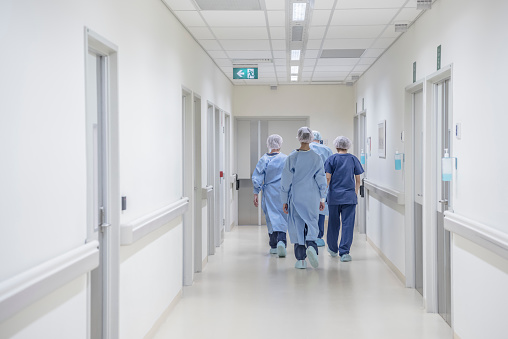 View from behind of four doctors in hospital corridor walking away from camera. Medical team in modern hospital corridor wearing surgical scrubs