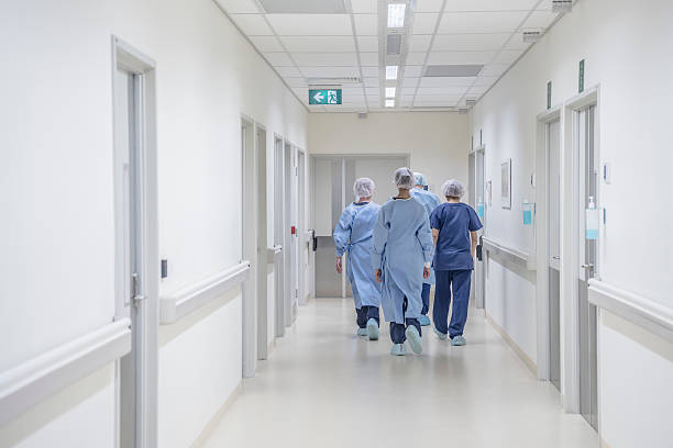 Rear view of surgeons walking down hospital corridor wearing scrubs View from behind of four doctors in hospital corridor walking away from camera. Medical team in modern hospital corridor wearing surgical scrubs hospital stock pictures, royalty-free photos & images