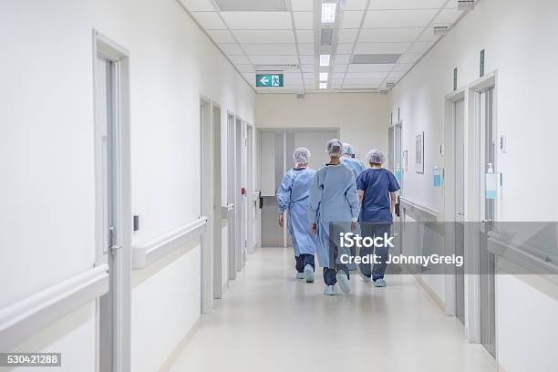 Rear View Of Surgeons Walking Down Hospital Corridor Wearing Scrubs Stock Photo - Download Image Now