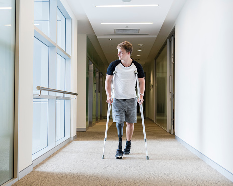 Disabled man with prosthesis in hospital corridor. Man with false leg walking in hospital using crutches