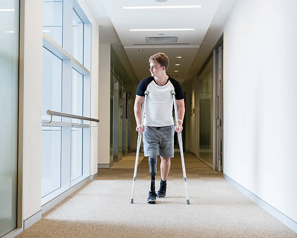 Young man with prosthetic leg on crutches Disabled man with prosthesis in hospital corridor. Man with false leg walking in hospital using crutches crutch stock pictures, royalty-free photos & images