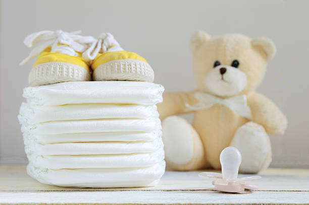 Some nappies on a white wooden table. Some nappies on a white wooden table. Sneakers, a pacifier and a teddy bear. Empty copy space for editor's text. group of babies stock pictures, royalty-free photos & images