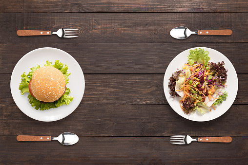 Fresh salad and burger on the wooden background. contrasting food.