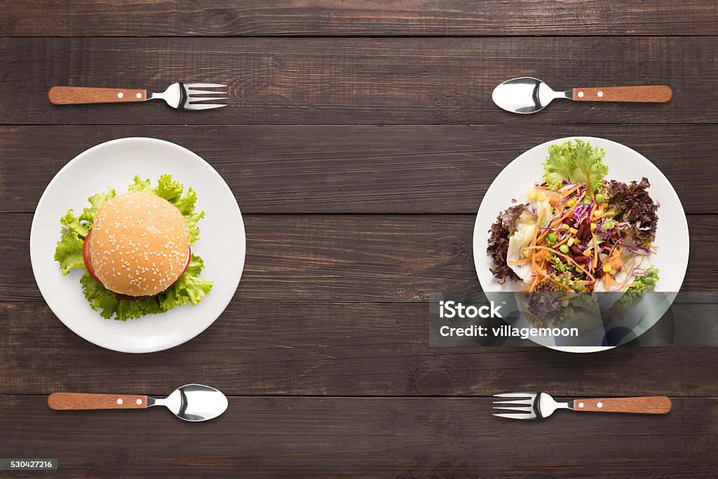 Fresh salad and burger on the wooden background. contrasting foo Fresh salad and burger on the wooden background. contrasting food. Burger Stock Photo