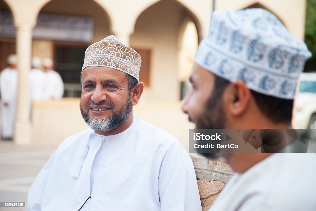 Men talking outside and looking friendly, Nizwa, Oman Adult omani man in traditional clothing; dishdasha and kummah cap, looking away at market in Nizwa, Oman. Oman Stock Photo