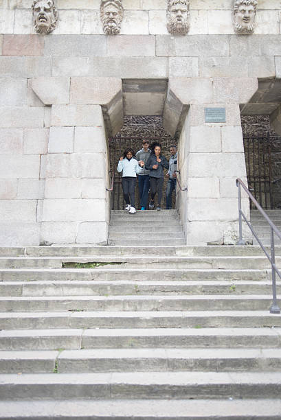 A mixed-race group of four young adult friends jogging under the famous Pont Neuf (the oldest bridge in Paris) overlooked by four stone heads.
