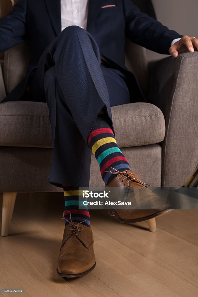 Man in suit with outstanding and funny colored socks Man wearing a navy blue suit and brown leather shoes with funny colored socks Sock Stock Photo