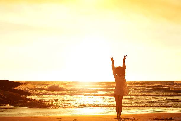istock Woman standing at beach with arms raised and peace sign 530430332