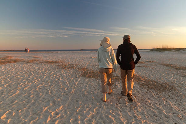 Wrightsville Beach, North Carolina, USA - November 13, 2015: A young couple talks off for a walk on a scenic beach with water in the background through the light of a golden sunset