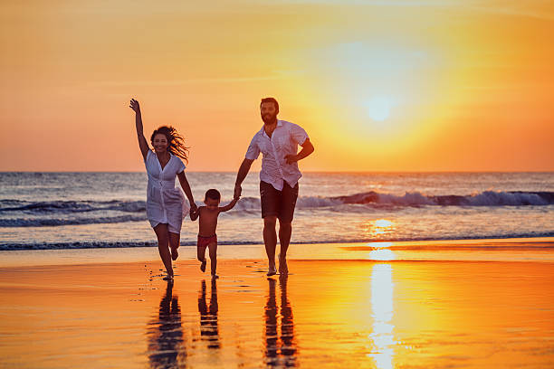 père, mère et bébé s'amuser sur une plage au coucher du soleil - usa travel sunset summer photos et images de collection