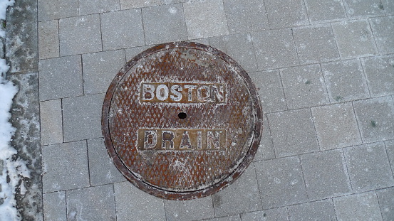 Boston, Massachusetts, USA - January 21, 2016: Rusty manhole cover holding out against winter snow and salt