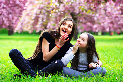 Happy beautiful young woman with girl in blossom park with trees and flowers.