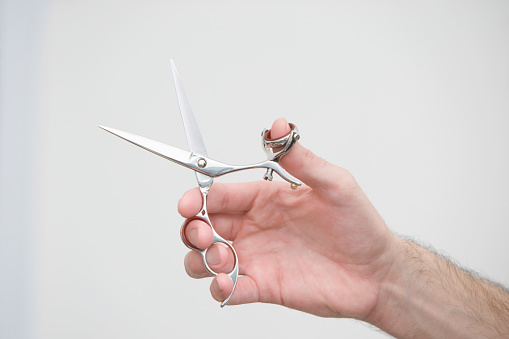 Cropped image of male hairdresser holding scissors in beauty salon