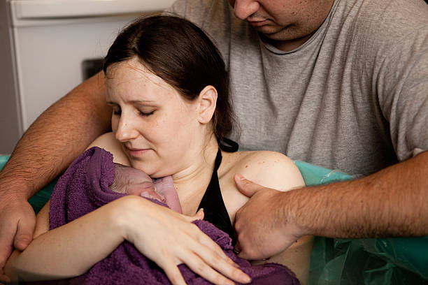 Husband Comforting Wife Holding Newborn after Home Water Birth Color photo of a husband comforting his wife while she holds their newborn baby in the water of a birthing tub immediately after a water birth at home. home birth photos stock pictures, royalty-free photos & images