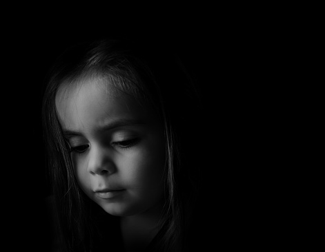 Low key Portrait of a young child. Sad looking girl is looking down.Picture is black and white.