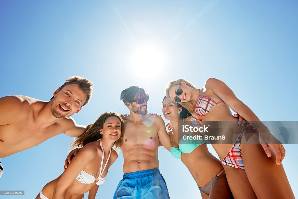 Embraced friends against the sky. Low angle view of happy young people enjoying in summer day together and looking at the camera. Copy space. Adult Stock Photo