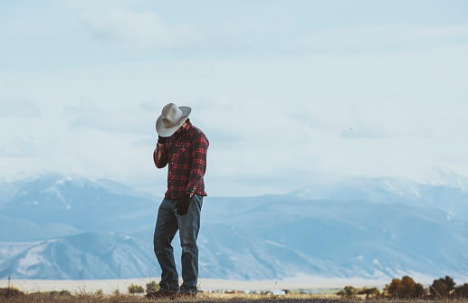 Cowboy talks on cell phone while standing with mountains in the distance