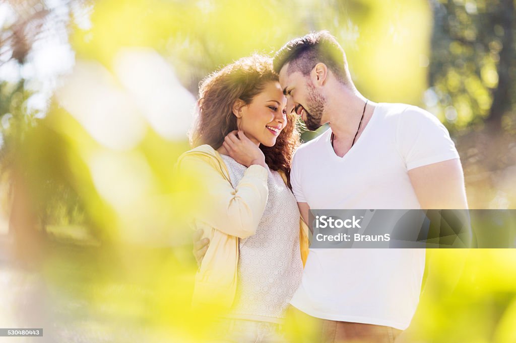 Couple in love. Happy young couple enjoying in their love outdoors. View is through the leaves. Adult Stock Photo