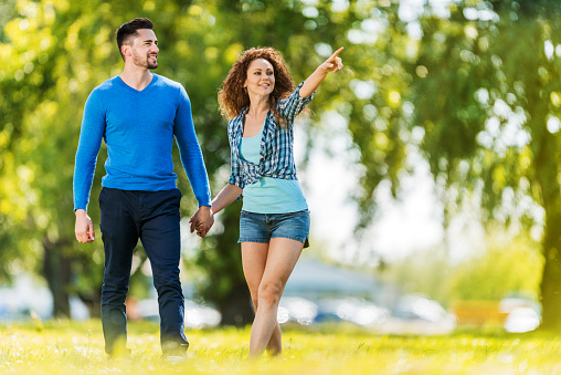 Young happy couple taking a walk in the park. Woman is pointing at something.