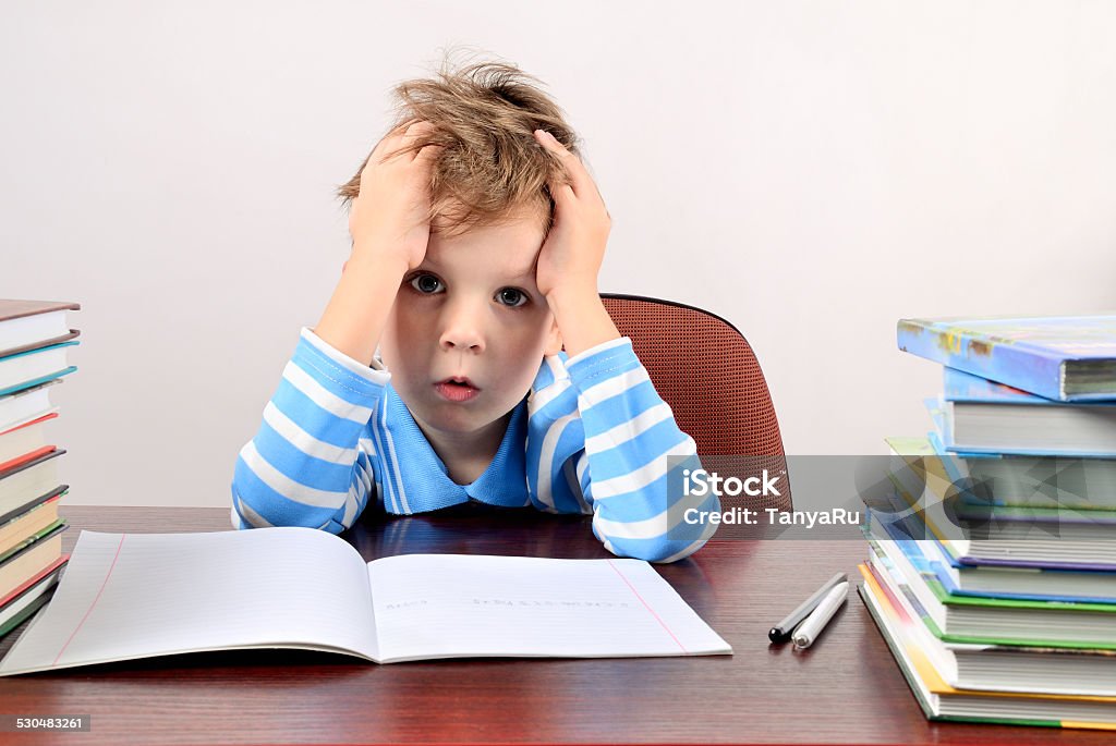 tired boy sitting at a desk and holding hands head tired boy sitting at a desk and holding hands to head horizontal Child Stock Photo