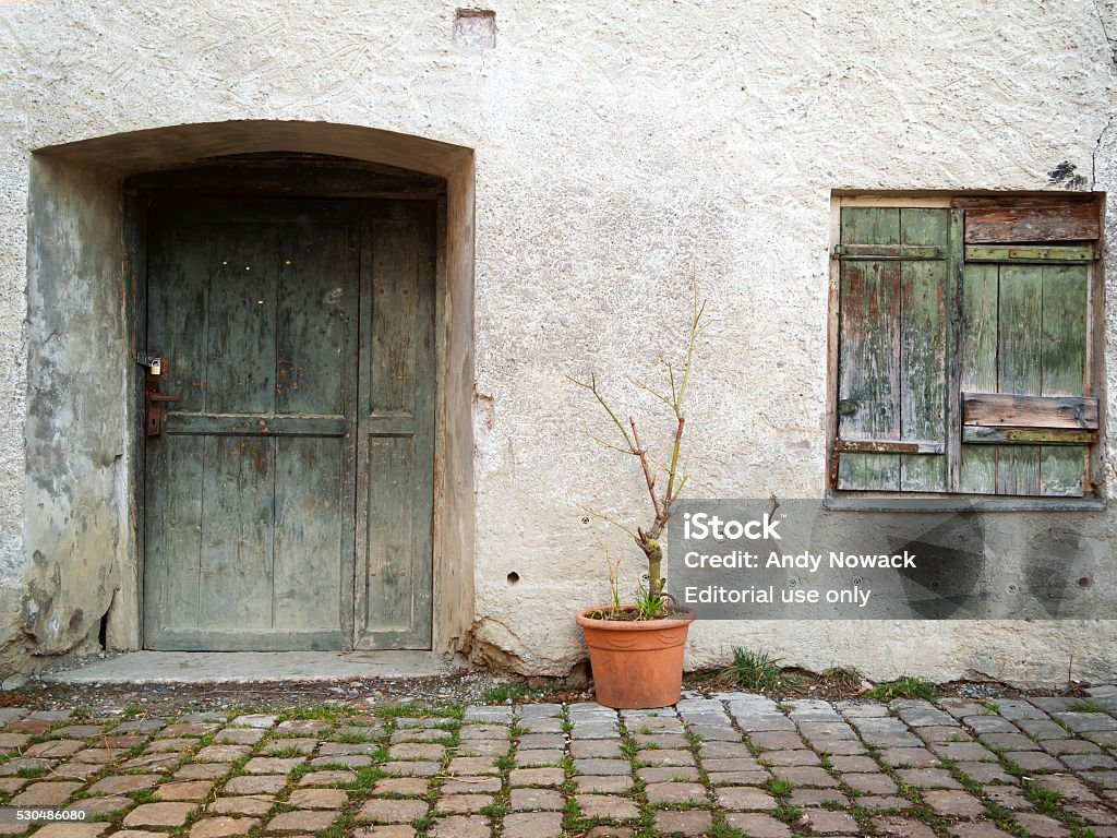 Facade of a House Fuessen, Germany - April 7, 2015: House facades in the old town of Füssen with old wooden door, shutters folded to and a standing between door and window flower pot with wilted plant Abandoned Stock Photo