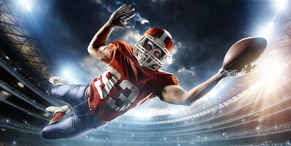 Professional football player catches a ball. The action takes place on professional stadium. The player wears unbranded sports uniform. There is artificial light on stadium together with sunlight.