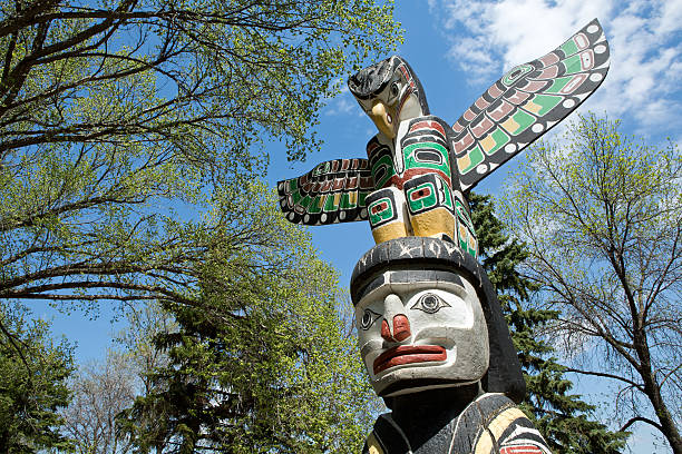 Kwakiutl Totem Pole at Wascana Lake in Regina Saskatchewan The Kwakiutl Totem Pole was carved from Western Red Cedar at Vancouver, British Columbia by Lloyd Wadhams of the Nimpkish Indian Band. It was gifted to the Province of Saskatchewan by the Government of British Columbia to commemorate their centennial year in 1971, and is one of twelve that was presented to Canadian centres. It is 4.9 metres high, 1.1 metres in diameter, and weighs approximately 1,588 kilograms. The predominant feature is a large thunderbird, a legendary being in North American Indigenous history and culture. For the Kwakiutl Indigenous people, it is particularly a symbol of family solidarity. regina stock pictures, royalty-free photos & images