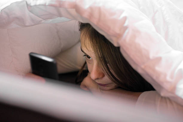 istock Girl using a mobile phone under the blanket 530490818