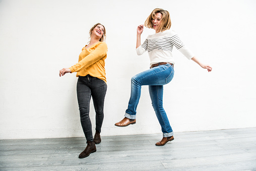 Cheerful blond young women jumping, front view, against white wall, Paris, France. Casual clothes, jeans, full lenght. Copy space. Nikon D800, full frame, XXXL. iStockalypse paris 2016.