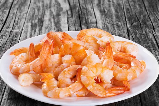 boiled tails of king shrimps on a white platter on an old rustic table, close-up, studio lights