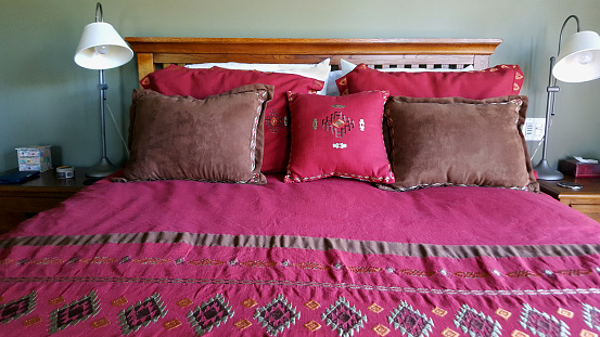 Close up of Embroidered comforter and pillows on bed. Mission style Oak bed and night tables.