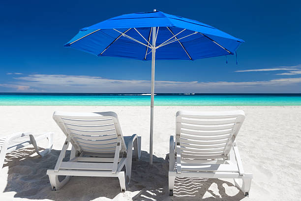 istock Caribbean beach with blue sun umbrellas and white beds 530505488