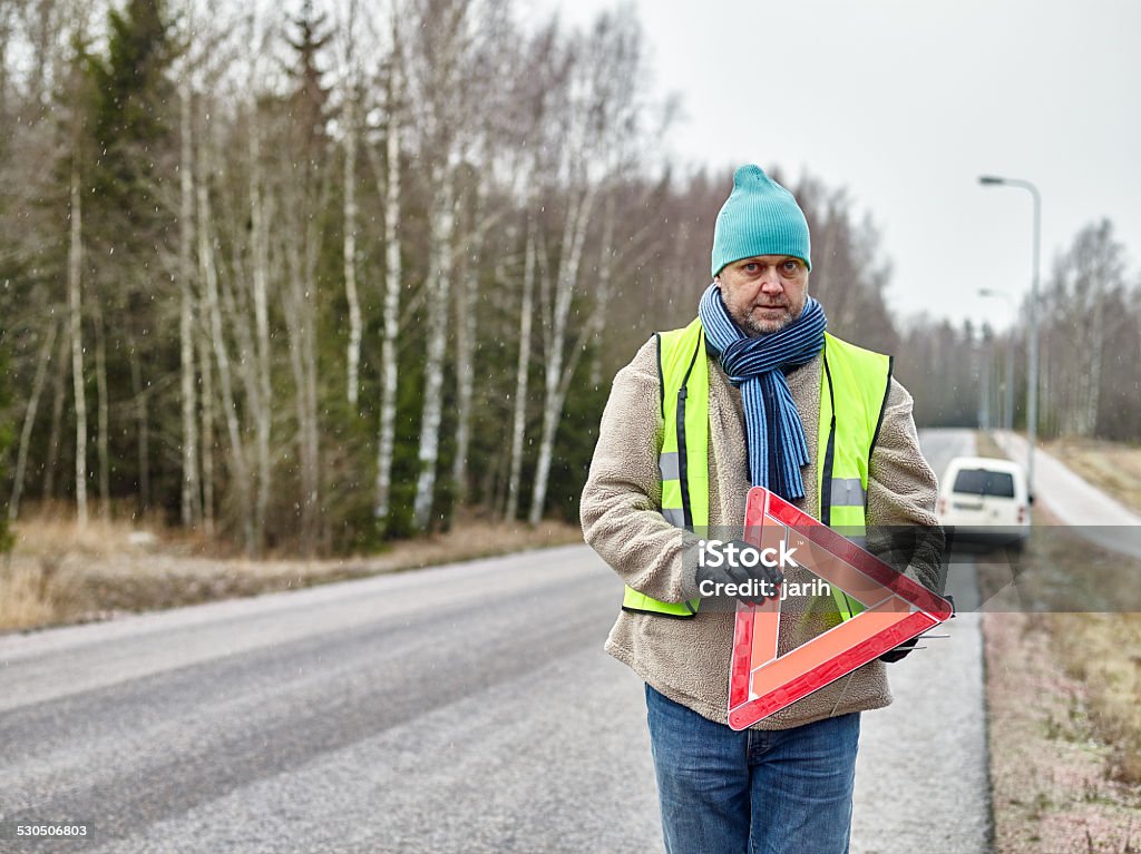 Male and warning triangle Mid adult man wearing reflector vest and he have a red warning triangle - road and vehicle on background Knit Hat Stock Photo