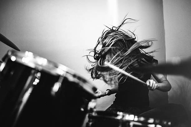 Girl Playing Rock and Roll Drums A 9 year old girl has fun playing a drum set in her room, working on songs for her band.  High contrast black and white image. musician stock pictures, royalty-free photos & images