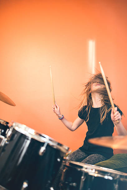 Girl Playing Rock and Roll Drums A 9 year old girl has fun playing a drum set in her room, working on songs for her band.  Bright sunlit bedroom with orange walls. drummer stock pictures, royalty-free photos & images